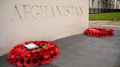 Two poppy wreaths lie in front of a stone memorial that has Afghanistan written on it.