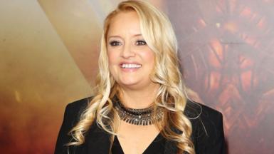 Lucy Davis smiling in a black jacket and necklace on a red carpet