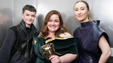 Owen Cooper and Erin Doherty standing either side of a grinning Jessica Gunning, who's holding her Bafta mask trophy