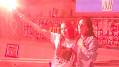 A girl, standing next to her mother, holds a red flare above her head.