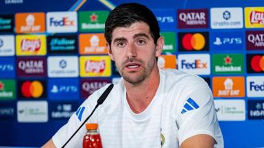 Thibaut Courtois is wearing a white t-shirt and speaking into a micrphone