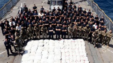 The crew onboard HMS Lancaster stood behind the pile of white bags of drugs.
