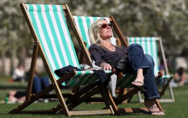 A woman sunbathes on a striped deck chair in a park