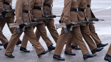 A shot of members of the armed forces marching and carrying rifles
