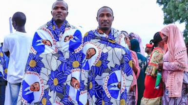 Two men who support Paul Biya wrapped in blue-patterned cloth with the face of Cameroon's president - Yaoundé, Cameroon