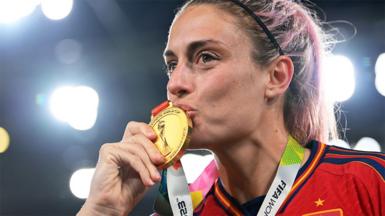 Alexia Putellas, wearing a red Spain football jersey, kissing a gold medal.