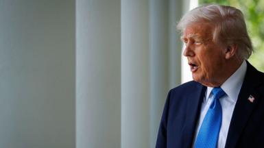 US President Donald Trump walks out of the Oval Office for a signing ceremony for the Take It Down Act, in the Rose Garden of the White House in Washington DC on May 19. He wears a blue suit and tie and appears to be saying something. 