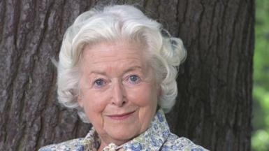 June Spencer, pictured in 2003, standing by a tree in a flowery dress