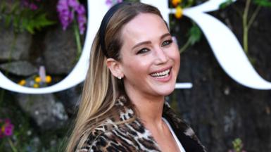 Jennifer Lawrence smiling at the Dior show wearing a black hairband and an animal print coat