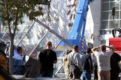 Men stand in front of a crane and a smashed glass structure in front of a railway station in Serbia