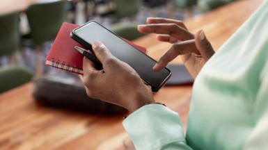 Woman types on phone while holding a notebook and a pen