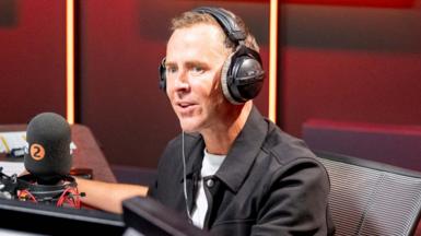 Scott Mills in the Radio 2 studio wearing headphones and a black jacket