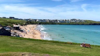 A wide sandy beach with lots of people on, and in the sea