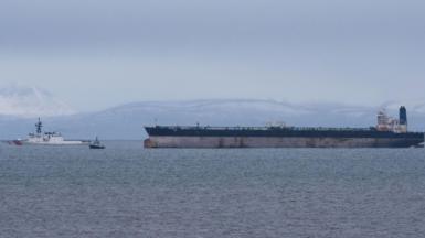 The large tanker is floating on calm water with a US Coast Guard ship in front of it.