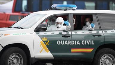 Men in hazmat suits inside a car with Guardia Civil written on the side and a SPANISH FLAG
