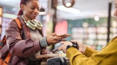 A woman pays for a book in a bookshop using her smartphone. The staff member at the till is holding up a card machine to the customer's phone