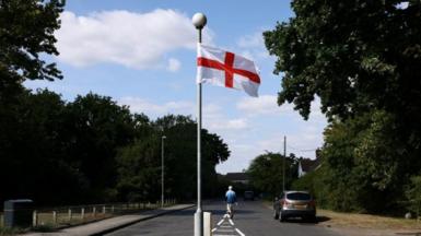 A St George's flag hangs from a lamppost on an empty street. 