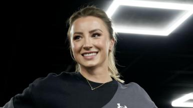 Vicky Williamson has her blonde hair in a pony and is smiling away from the camera. She has a black and grey sports top on.