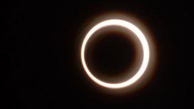 A 'ring of fire' eclipse - a golden circular ring of sunlight eclipsed by a dark shadow caused by the Moon obscuring the Sun against a dark black sky, taken in Rapa Nui, Chile on 2 October