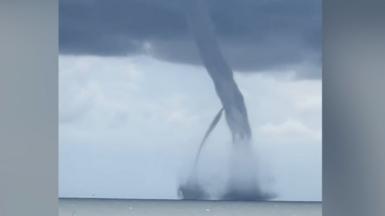Two large dark grey waterspouts reach up into a dark cloud above the sea off the Italian coastline.
