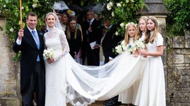 The bridge and groom smiling outside the church, as the three bridesmaids hold the train of her dress.