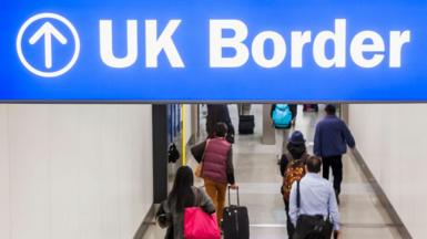 A blue sign reading 'UK border', with people waking underneath