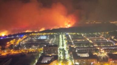 Aerial of red flames burning in mountain next to houses