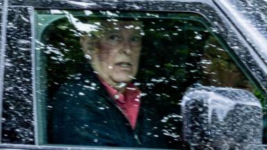 Andrew Mountbatten-Windsor wearing a pink shirt and dark jacket pictured behind a rain-spattered window of his vehicle