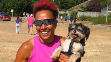 Dame Kelly Holmes is holding a tiny dog and smiling as the dog sticks its tongue out