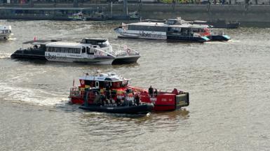 A fire boat is towing a black rigid police vessel on the River Thames in central London.