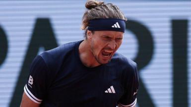 Alexander Zverev, wearing a black Adidas t-shirt and headband with his hair tied back, roars with his mouth open