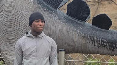 Eghosa Ogbebor pictured standing in front of a dinosaur sculpture