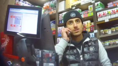 A man on his phone behind the counter of a corner shop