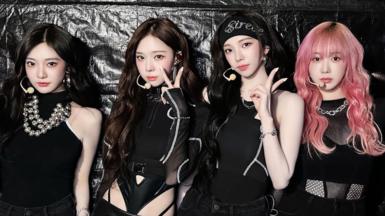 Korean girl band aespa, dressed in black, throw up peace signs while posing backstage at a concert in Seoul