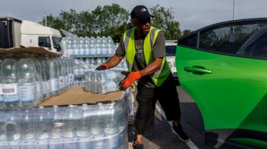 A person loads a green car with water bottles during a handout event organised by Southeast Water during a water shortage following the hot weather in May.