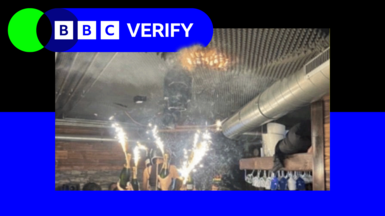 A branded image with the BBC Verify logo, with a blue border surrounding an image of sparklers attached to champagne bottles being held up by people in the Swiss ski resort bar just before the fire started - with a small orange patch of fire seen on a foam ceiling above the sparklers.