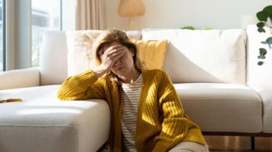 Woman having headache and holding her head while sitting on the floor at home