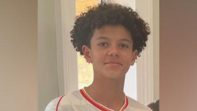 Noah smiling at the camera. He is wearing a white football shirt with red edging and has short curly hair.