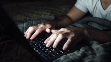 An anonynous man, lying on a bed and using a laptop computer