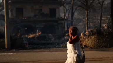 A woman reacts as she walks near a burnt house during a wildfire in Peristeria area