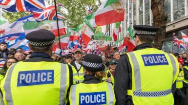 Rear view of three police officers with crowd in front