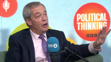 Nigel Farage gesticulates in the Political Thinking studio. He wears a dark navy suit with a blush pink shirt and a violet tie.