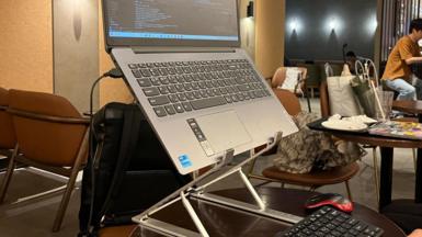 A laptop set up on a stand with a keyboard and mouse on a table in a Starbucks cafe.