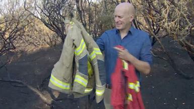 BBC South environment correspondant in the New Forest holding two different firefighter jackets.