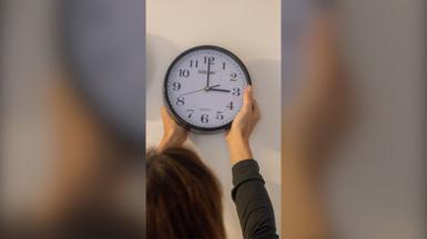 Woman seen from behind putting a clock back on the wall.