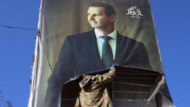 An anti-government fighter tears down a portrait of Bashar al-Assad in Aleppo.