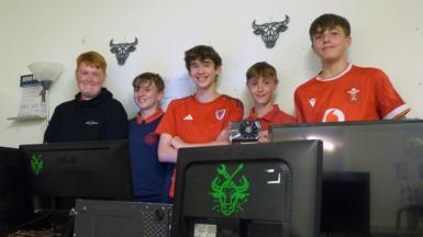 Grwp o fechgyn yn sefyll tu ol i gyfrifiaduron