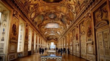 Image shows an overall view of the Apollon Wing gallery in the Louvre which is a highly ornate, gold-gilded room, with an embellished vaulted ceiling, and tapestries, which house the French Crown Jewels.