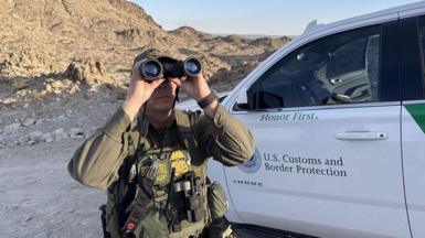 Border Patrol agent using binoculars next to his vehicle in a desert area of El Paso on 5 November, 2025. 