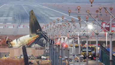 The crashed Jeju Air plane that went off the runway lies at Muan International Airport, in Muan, South Korea, with emergency vehicles nearby